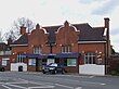 A brown-bricked building with a black roof and a blue sign that reads "CHIGWELL STATION" in white letters all under a white sky