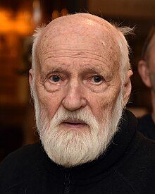 A portrait of an elderly man, balding with a white full beard and wearing black.