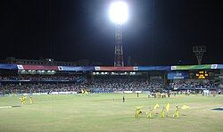 View of a cricket stadium. It has some players in yellow outfit and they are folding yellow flags.