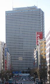 A building-lined street acts as a corridor, leading directly to the grey, rectangular, window-dotted facade of a high-rise building