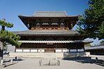 Large wooden building with a hip-and-gable roof, two enclosing pent roofs and an open gallery with handrail on the upper floor.