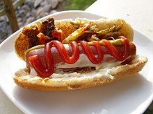 Hot dog on toasted bun with kimchi, mustard, mayo and ketchup on a white plate.