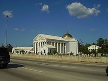 Large Greco-Roman style church sitting along a road within a residential area.