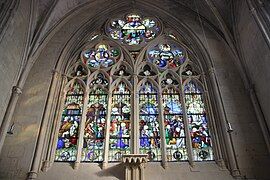 Low-angle view of the Virgin's stained glass window with six sections above with numerous figures and three rosettes above.