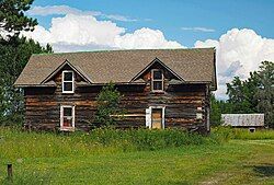 One-and-a-half story log house with peaked dormers, with small barn in background