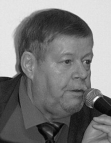 Sepia photo: Face shot of Arto Paasilinna, speaking in a microphone.