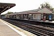 A grey railway platform with a railway track running down the middle and a rectangular, red sign reading "WHISTLE" in white letters