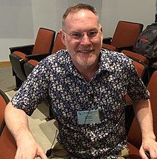 Carpick sitting and smiling in an indoor auditorium setting.