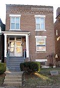 tall narrow 3 story brick building with borrom window partially below ground; steps up