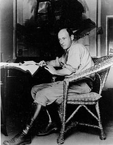 DeMille posing on a chair with a pen in hand