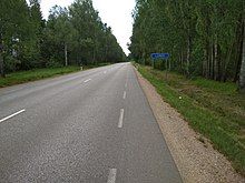 Picture of a road with trees lined on either side. There is a blue sign on the right side of the road that says “Londi”.