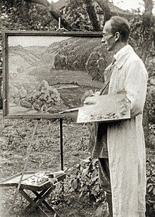 A black and white photograph of Walter Gotsmann standing outside in a garden at an easel, holding a paintbrush and palette. On the easel is a finished painting of a countryside scene.