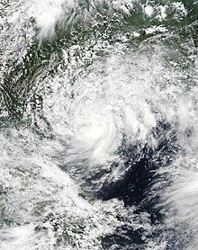 A photograph of a tropical storm near the coasts of southwestern China and northeastern Vietnam. Thick convection spirals around the center, especially on the southern side of the circulation; a large region of high, puffy clouds fans out to the northwest, north, and northeast of the center.