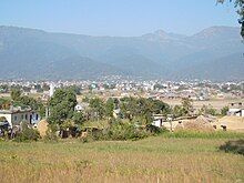 Small rural houses behind some brown grass against a mountain backdrop; A view of Surkhet valley from Latikoili