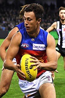 A man in a white shirt and maroon shorts stands on grass