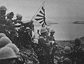 alt=Historic photograph of Japanese troops raising the Imperial battle flag on Kiska Island.