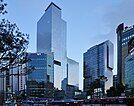 Several modern blue glass skyscrapers are visible. It is the early evening and a row of buses can be seen at the bottom of the photograph.