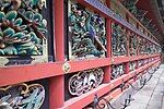 Wooden wall with red beams and colored carvings of plants, peacocks and other birds.