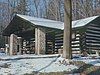 A snow-covered log cabin with a porch supported by stone pillars