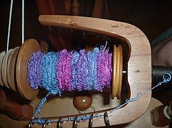 A reel of handspun bouclé yarn in blue, purple and pink. The effect yarn has created a densely-packed series of small loops.