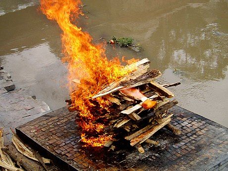 A Hindu cremation rite in Nepal. The samskara above shows the body wrapped in saffron red on a pyre.