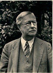 Older gentleman in suit, tie, and glasses with neatly trimmed hair and moustache