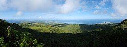 panorama of Saipan. There are green hills in the foreground, towns and beaches in the midground, sea and clouds in the distance.