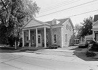 A black and white photograph of the same building from roughly the same angle. Part of another house is visible to the right.