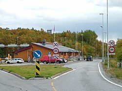 Storskog border station from the Norwegian side. Border posts are visible between the building and the dark van. A Russian watch tower rises on the hill in the background.