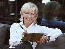 Blond-haired woman in dark coloured shirt smiling outdoors