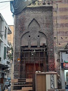 Photo of a doorway with painted red and black brickwork forming geometric patterns and with a wooden door