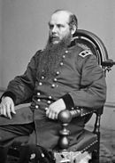 Black and white photo of a seated man in a dark military uniform with two stars on his shoulder tabs. He is balding and has a long beard.