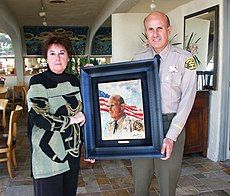 Rita Asfour handing Sherriff Lee Baca his portrait that Rita Asfour painted of him