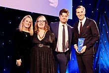 Colour photograph of members the ITV News team posing onstage with their AIB award.