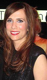 A brunette woman wearing a black dress smiles