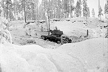 A Soviet light tank, seen from its left side, is described by the Finnish photographer as advancing aggressively in the snowy forested landscape during the Battle of Kollaa.