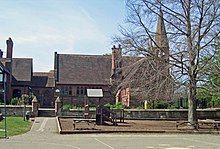 A stone building with a projecting bay, a tall chimney and a slim spire