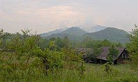 A green landscape with mountains in the back and a house towards the right.