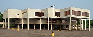 A white three-story building, where portions of the second and third stories are suspended over the parking lot on cylindrical supports