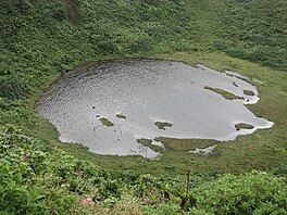 A crater covered in tropical vegetation, with a lake in the middle. The photo is taken from above.