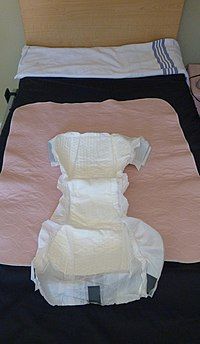 An adult diaper and a pink incontinence pad laid out on top of a single bed