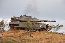 A main battle tank on a hill. A soldier is in the open hatch above the turret.