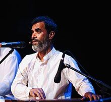 Medium close-up of Raj Mohan standing with a microphone in his face