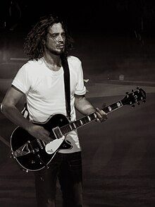 black-and-white image of Chris Cornell wearing a white t-shirt, standing onstage, playing an electric guitar