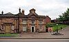 A sandstone building in two storeys, its façade including a Pediments with a clock above, and a balustraded parapet