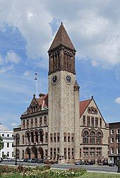 A brown and tan brick building with dark brown trim. The building has a tall bell tower on the nearest corner.