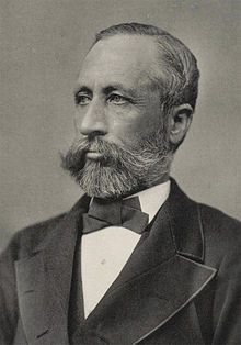 Head and shoulders photograph of a man in a Victorian suit. He has a beard, a large mustache and is slightly balding. He wears a serious expression and is looking slightly to the right.