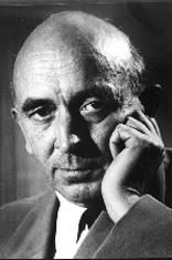 Publicity shot of clean-shaven man with receding hair and strong features. He is leaning his chin on the heel of his hand, and looking intently into camera