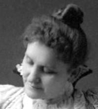 a head shot of a white woman with a high collared dress, looking down and to the left