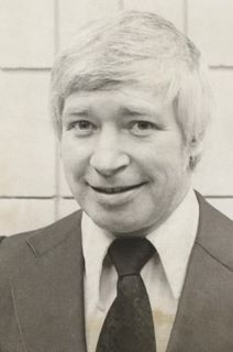 Black and white photo of a middle-aged man with grey hair, wearing a dark-coloured suit and tie, with a white dress shirt.